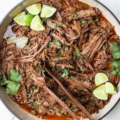 Mexican barbacoa garnished with limes and cilantro.