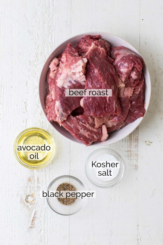 A beef roast cut into large chunks shown with avocado oil, salt and pepper.