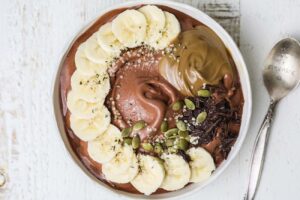 A thick chocolate smoothie topped with fresh fruit, seeds, and nut butter.