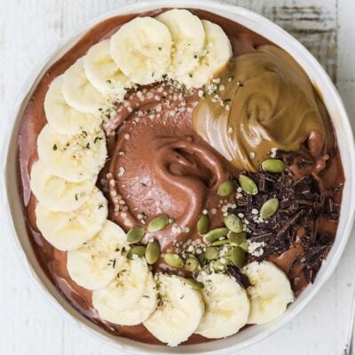 A thick chocolate smoothie topped with fresh fruit, seeds, and nut butter.