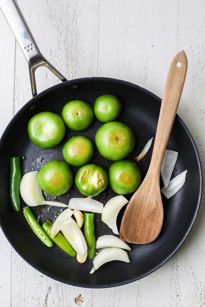 Tomatillos, onions, garlic, and chilis softening in a skillet.