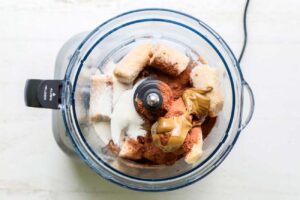 Frozen bananas, cacao powder, and sunbutter shown in a food processor.