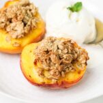 Two peaches in a bowl topped with an oatmeal crisp and served with ice cream.