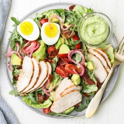 A green goddess cobb salad with chicken shown with a container of avocado green goddess dressing.