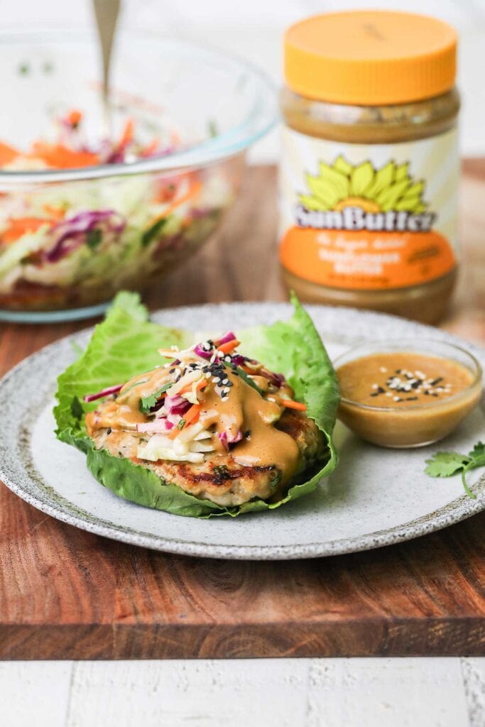 Thai Chicken burgers on a lettuce wraps sitting next to a jar of sunbutter.