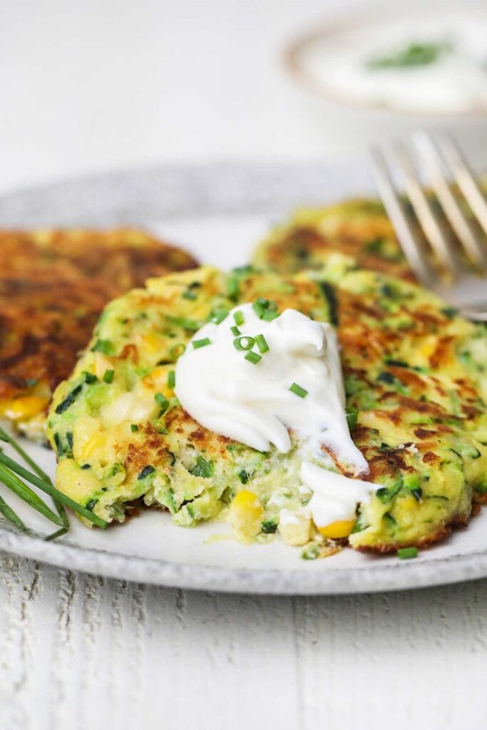 A zucchini fritter topped with sour cream with a bite taken out of the side.