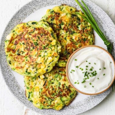 Zucchini and corn fritters shown topped with chives and served with sour cream.