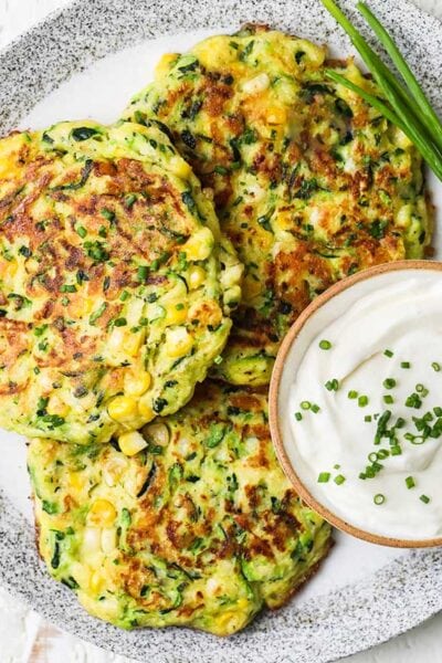 Zucchini and corn fritters shown topped with chives and served with sour cream.