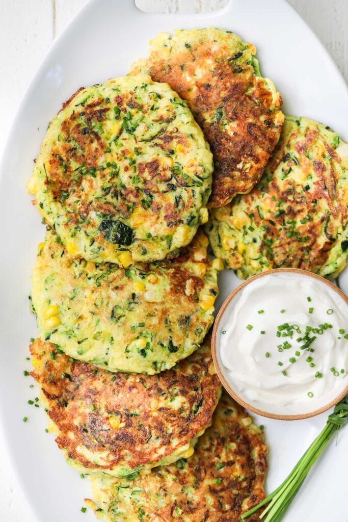 A platter of zucchini and corn fitters shown with sour cream.