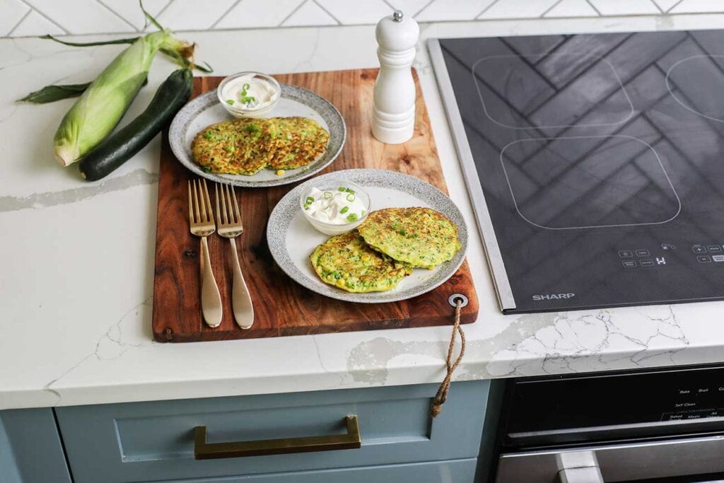 Two plates of zucchini fritters sitting near the Sharp Induction Cooktop.
