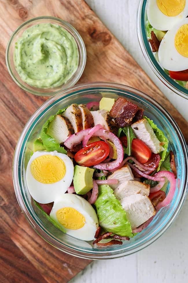 Salads topped with hard boiled egg, bacon, and chicken.