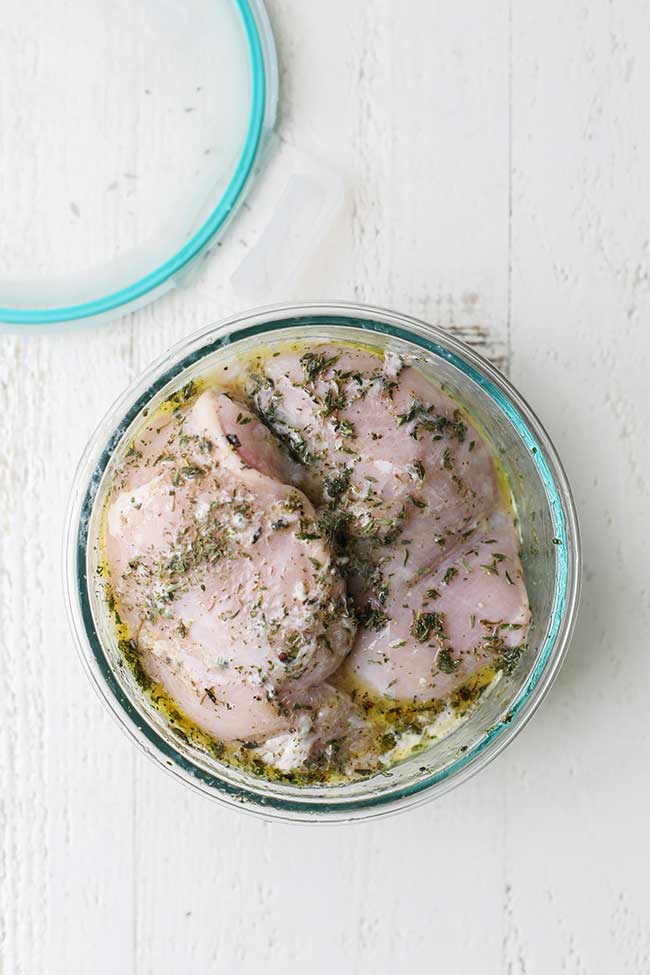 Chicken in a container with marinade ingredients.