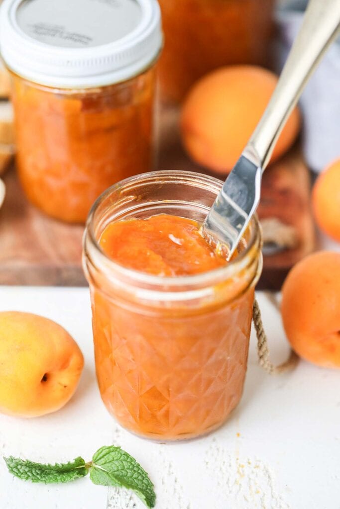 A knife sticking into a jar of vibrant orange apricot jam.