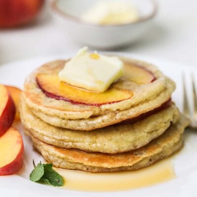 A stack of gluten free peach pancakes topped with butter and syrup.