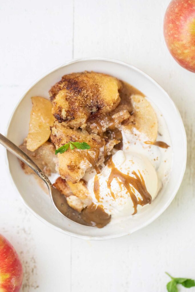 A bowl of hot apple cobbler with vanilla ice cream and caramel sauce.