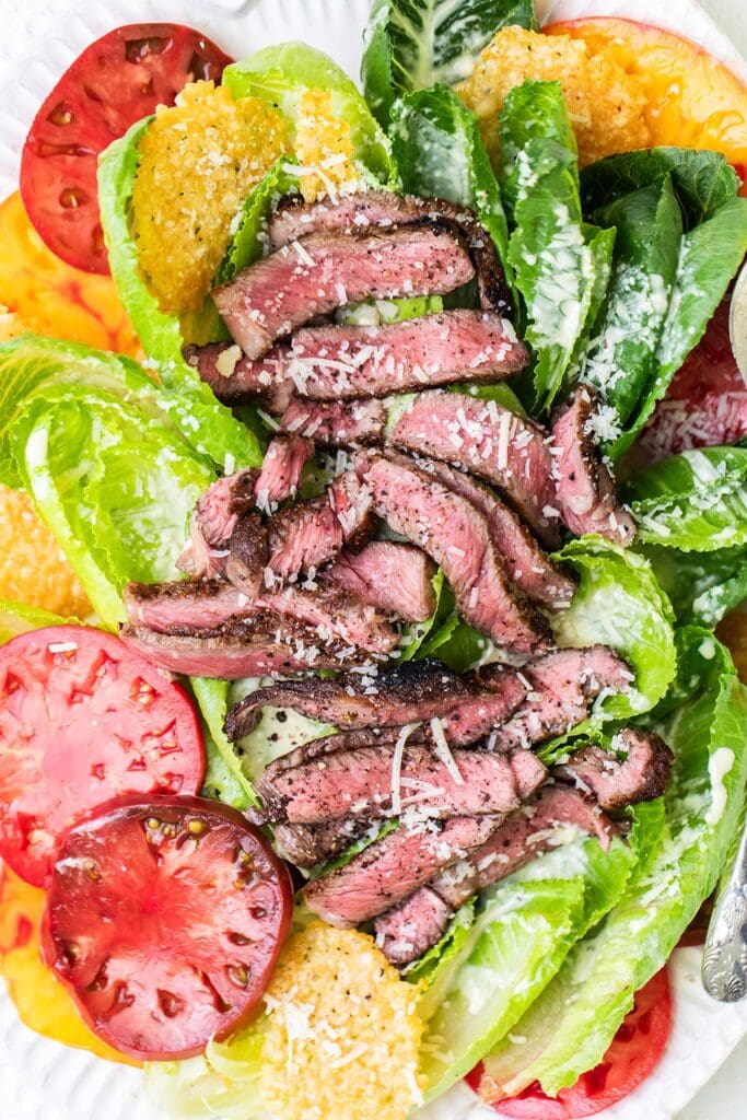 A steak caesar salad with large slices of heirloom tomatoes.