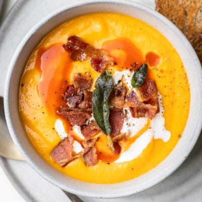 A bowl of butternut squash soup shown garnished with bacon and served with toast.
