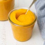 A jar filled with pumpkin puree with a spoon sticking out of the top.