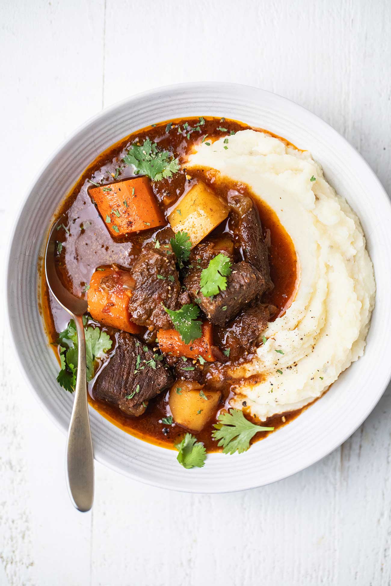 A bowl of Moroccan Beef Stew served over a bed of mashed potatoes in a white bowl.