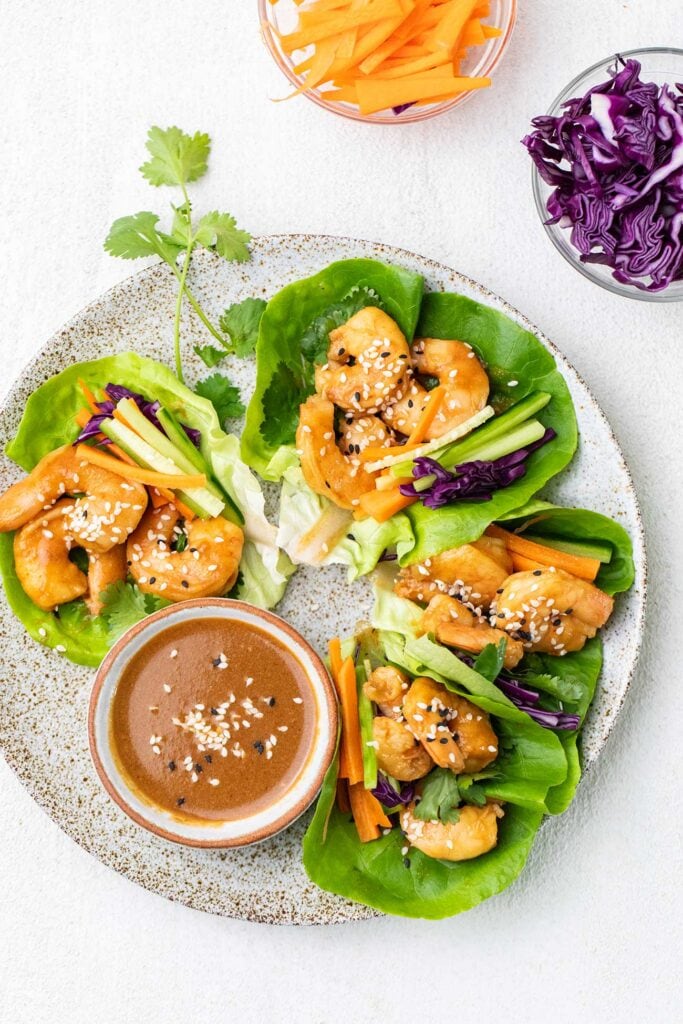 A plate of shrimp lettuce wraps shown with a spicy sauce and shredded vegetables.