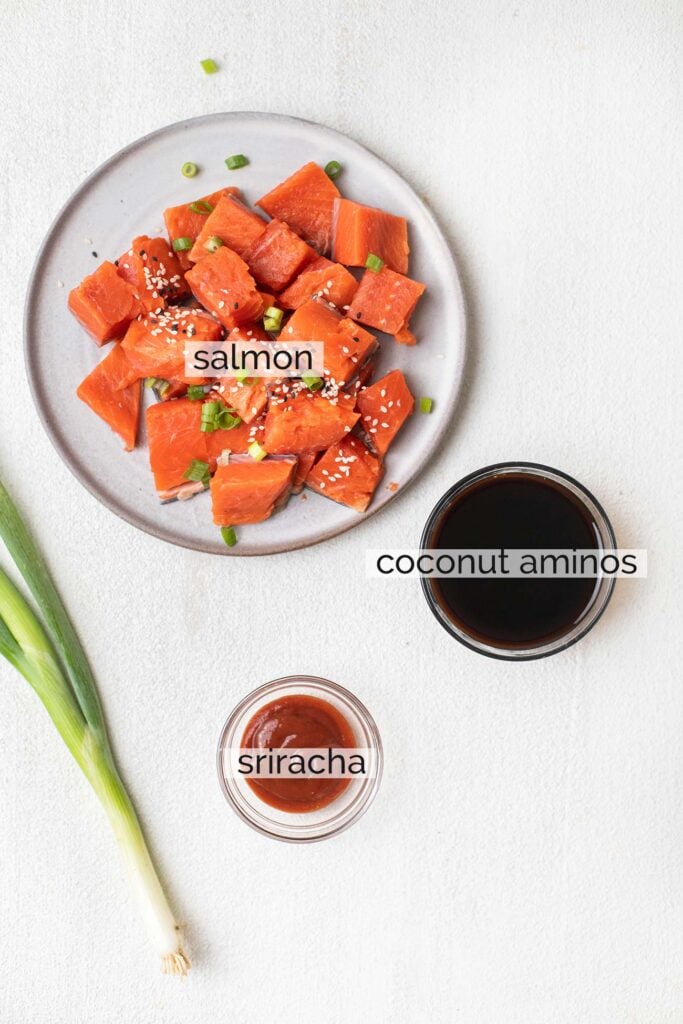 A plate of salmon cut into chunks with a bowl of coconut aminos and some sriracha, showing how to marinade the salmon.