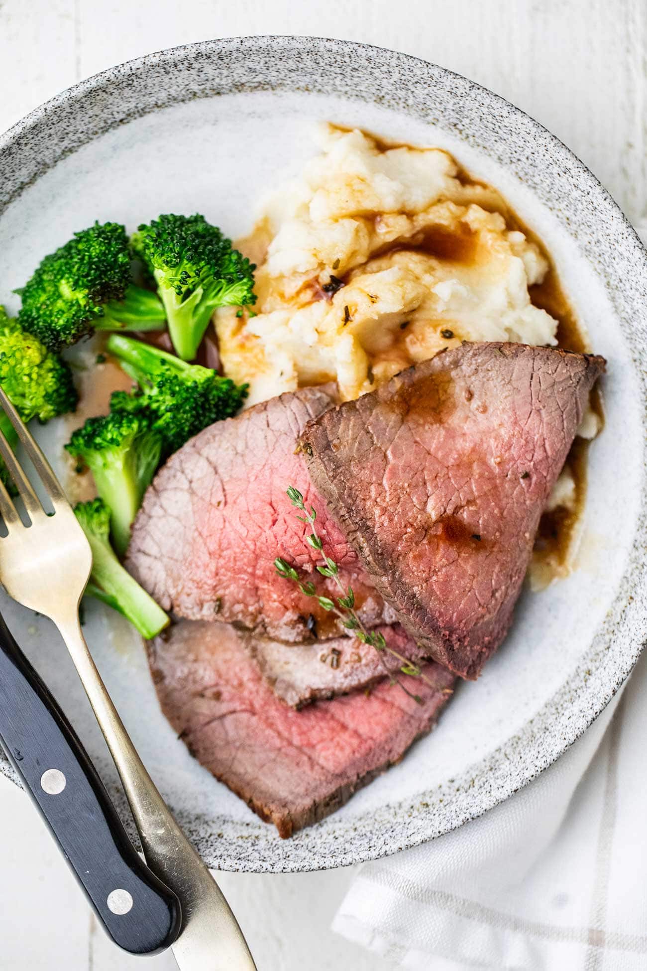 A plate shown with mashed potatoes, broccoli, and thinly sliced beef.