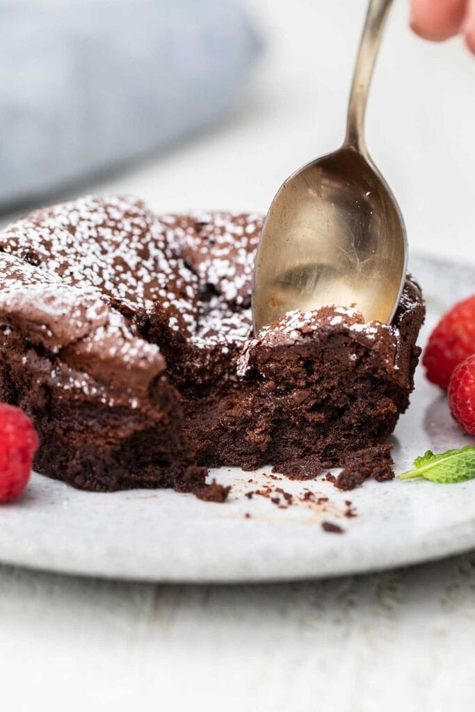A spoon taking a bite out of a souffle cake garnished with powdered sugar.