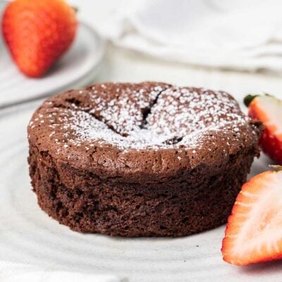 A chocolate souffle cake dusted with powdered sugar and served with strawberries.