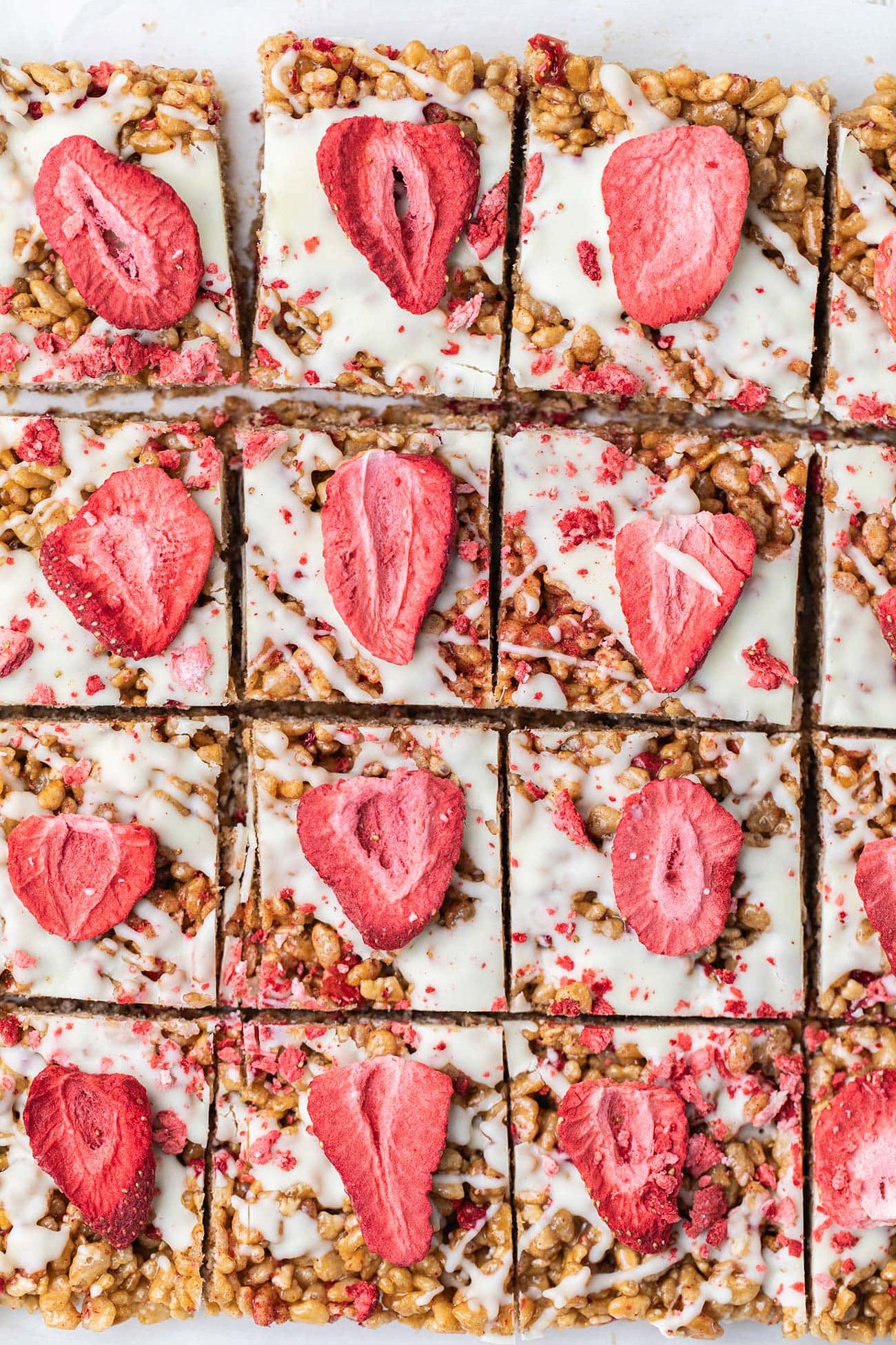 A batch of strawberry rice krispies treats cut into squares and topped with white chocolate and dried strawberries.
