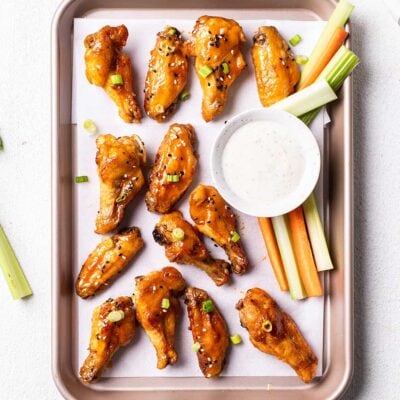 A baking pan with hot wings garnished with carrot and celery sticks and a dish of bleu cheese dressing.