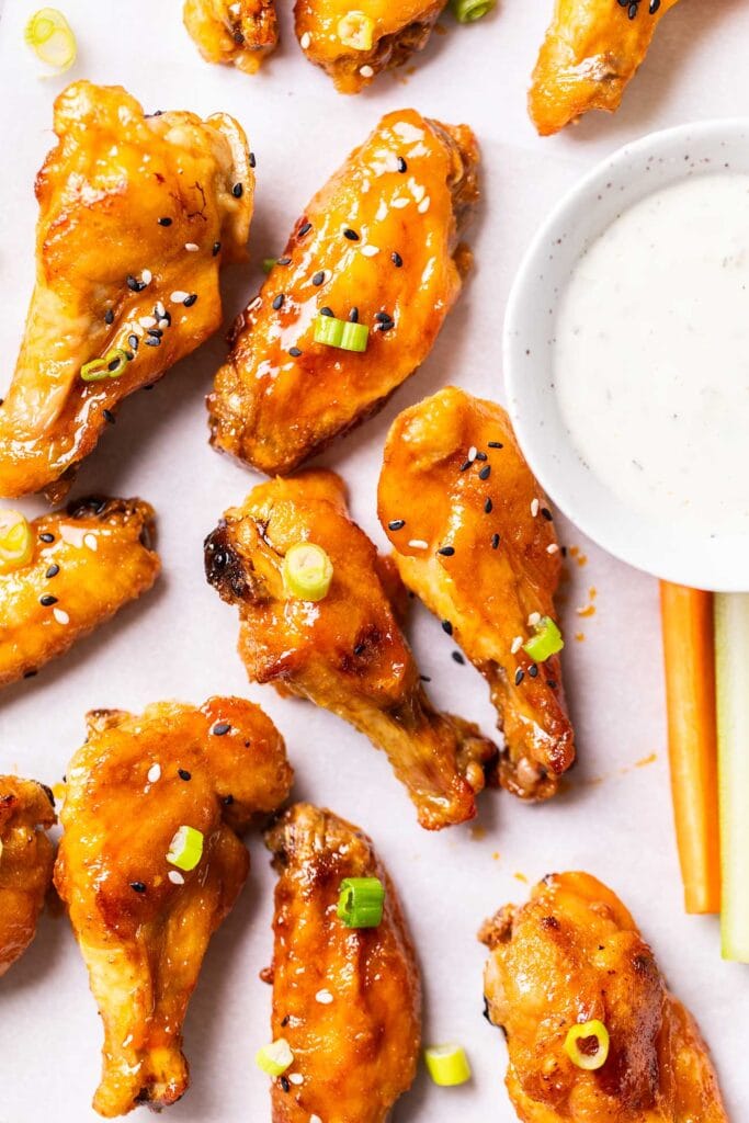 A baking pan with hot honey chicken wings garnished with green onions and sesame seeds.