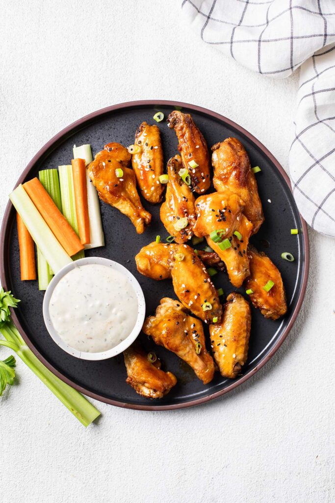 A black plate with hot wings garnished with carrots, celery, and bleu cheese dressing.