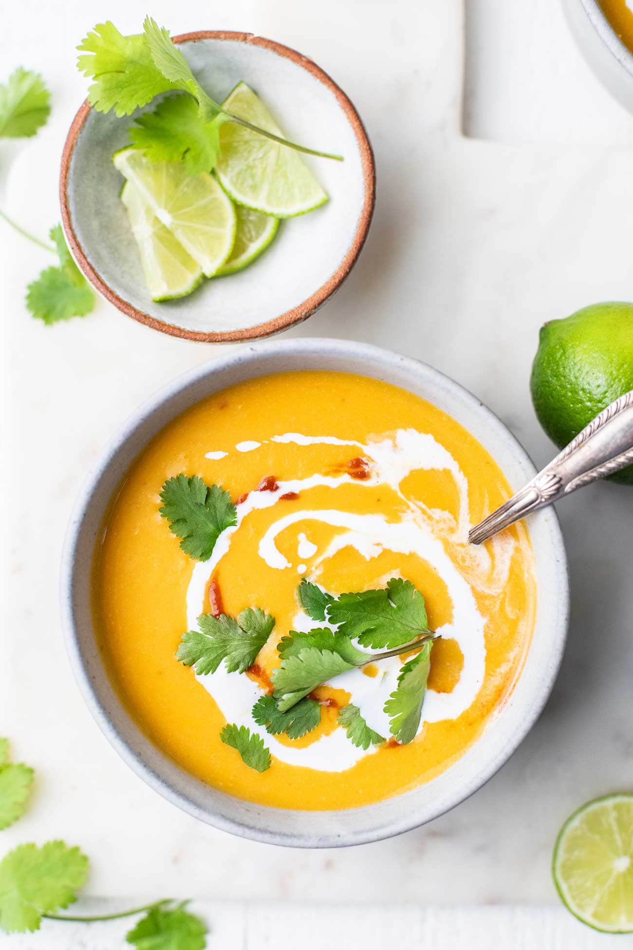 A bowl of Thai butternut squash soup garnished with cilantro and coconut milk, sitting next to a small bowl of limes.