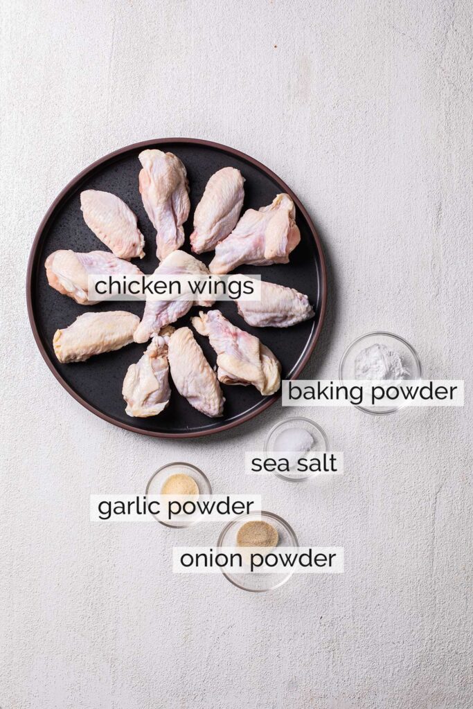 A plate of raw chicken wings shown with the ingredients for the spice coating.