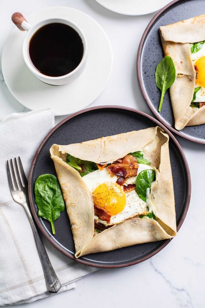 Crepes bretonnes shown filled with egg, spinach and bacon on a black plate.