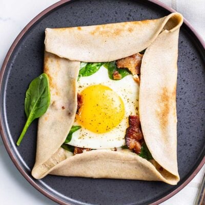 A buckwheat crepe filled with egg, spinach, cheese, and bacon shown on a black plate.