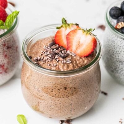 A jar of chocolate protein chia seed pudding shown garnished with cacao nibs and a strawberry.