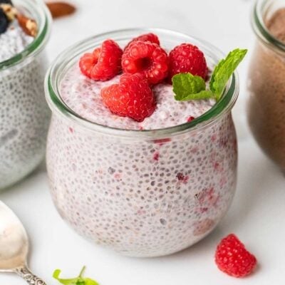 A jar of raspberry chia protein pudding in front of jars of vanilla and chocolate protein chia pudding.