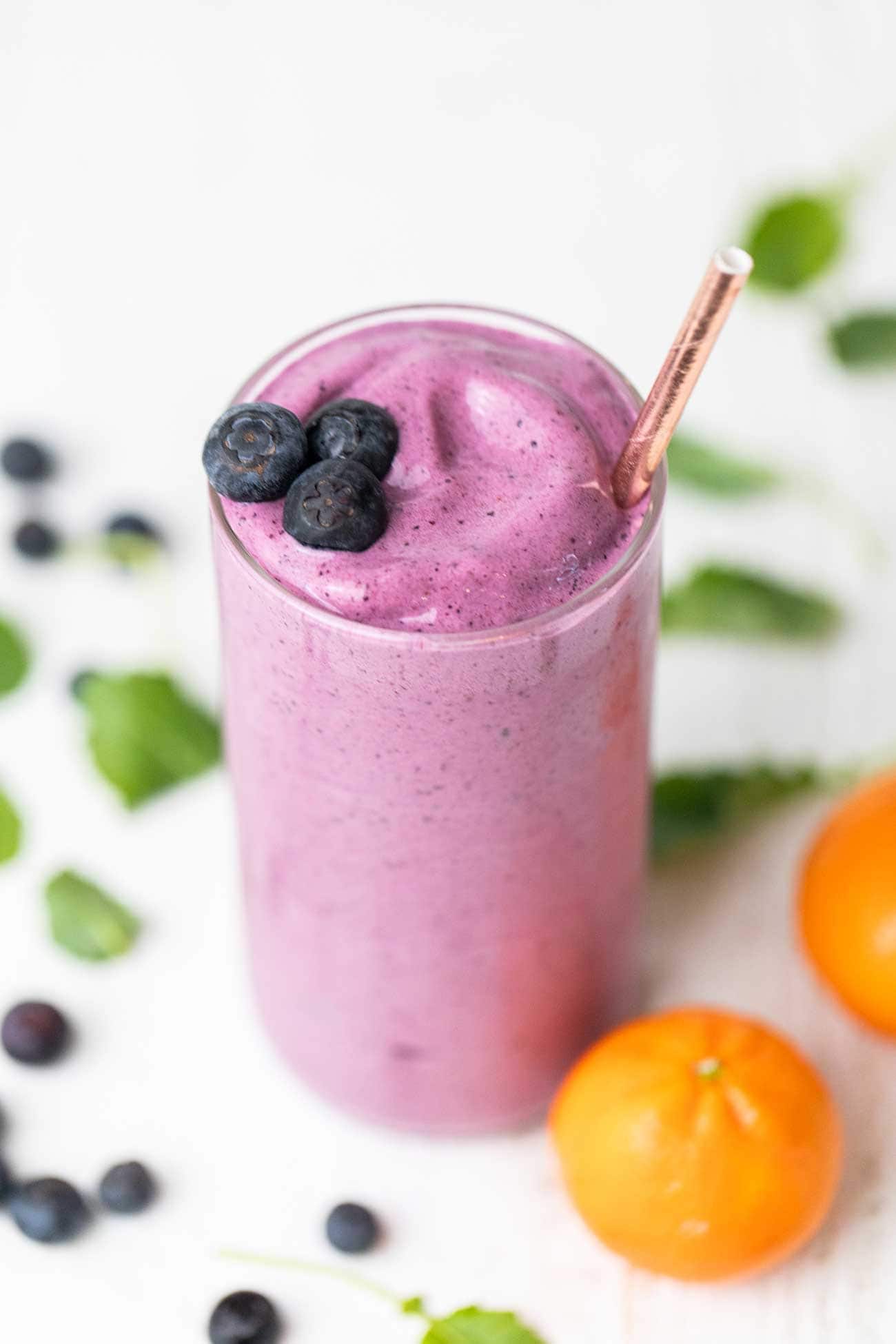 A thick and creamy smoothie made with cottage cheese and blueberries shown in a glass with a gold straw.