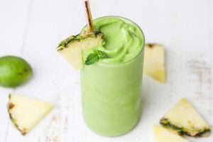 A vibrant green smoothie shown with wedges of pineapple sliced around it.