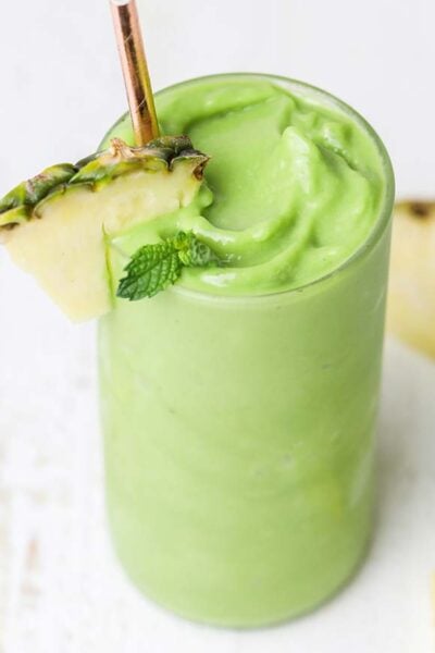A vibrant green smoothie shown with wedges of pineapple sliced around it.