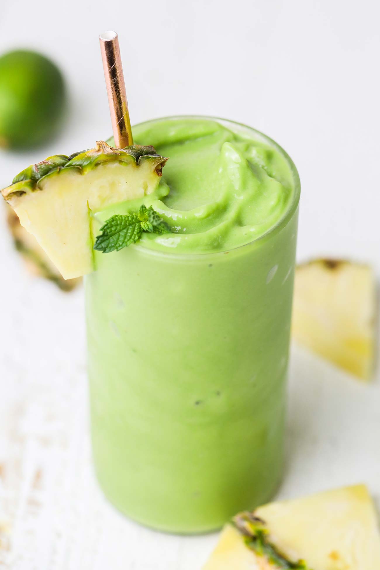 A thick, vibrant green smoothie in a glass garnished with a pineapple wedge.