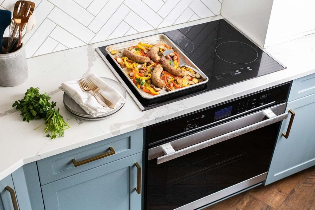 A sheet pan with sausages, onions, peppers and potatoes sitting on top of the Sharp Convection Oven.