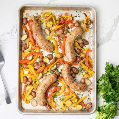 A sheet pan shown with 4 Italian sausages, peppers, onions, and baby potatoes.