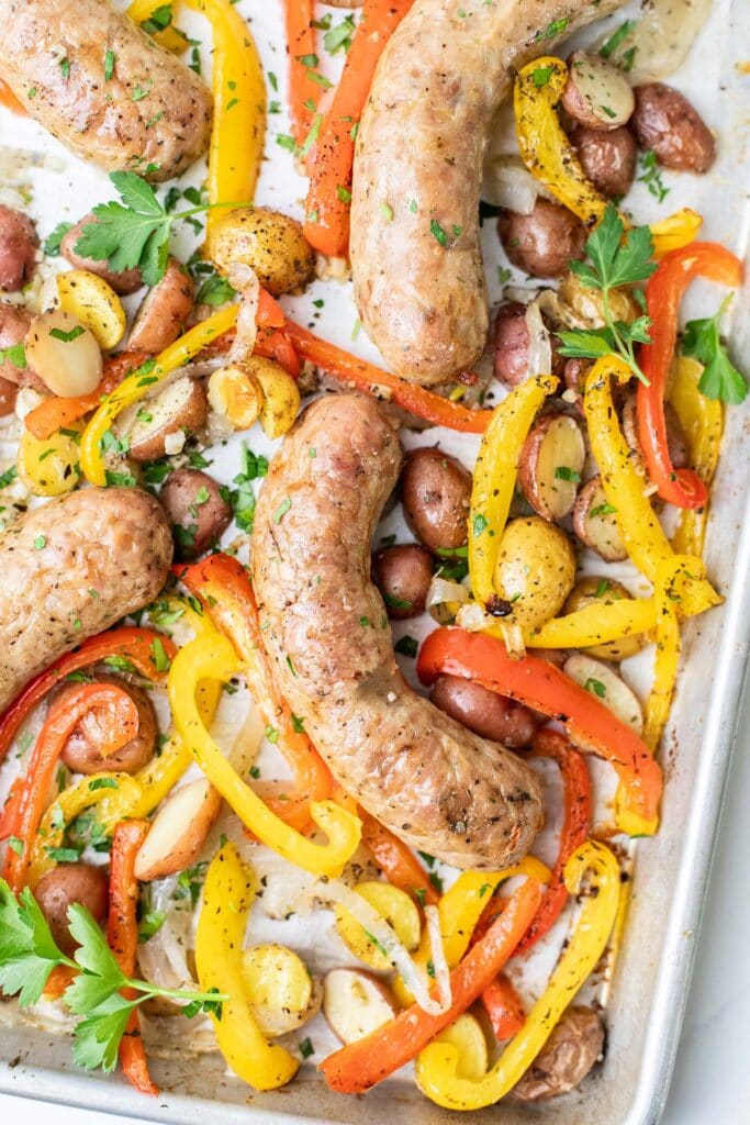 A sheet pan with baked italian sausages, onions, peppers, and potatoes.
