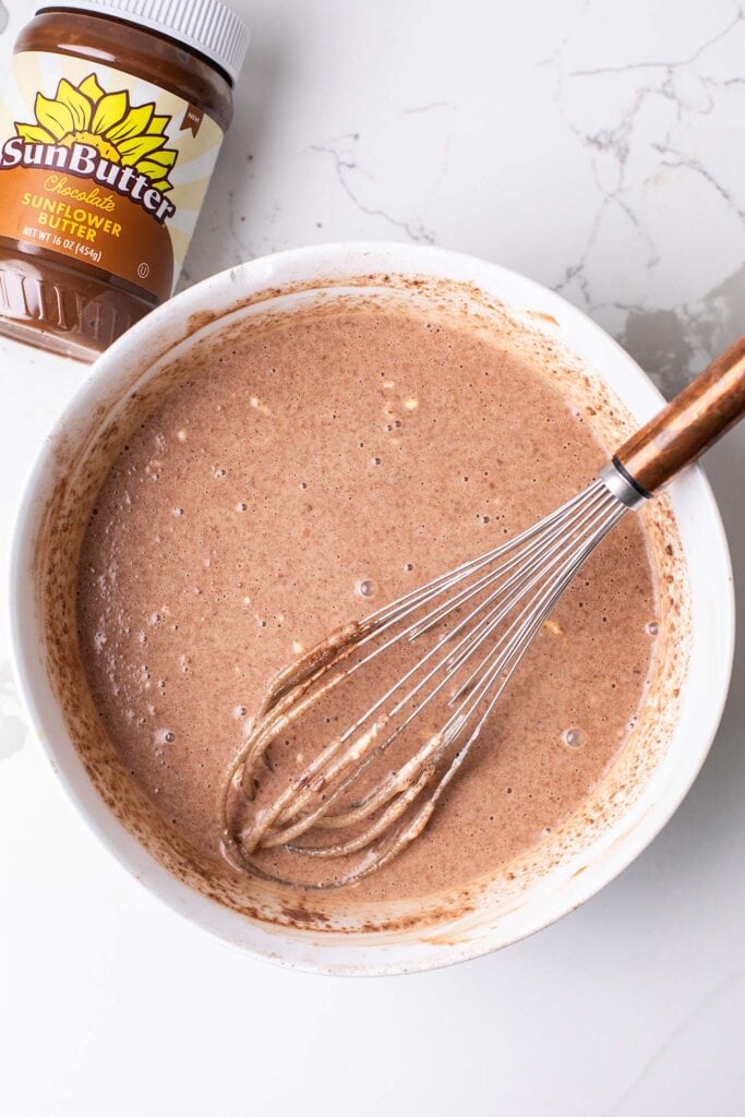 A large bowl shown with almond milk, greek yogurt, and cacao powder whisked together, and then the same bowl shown with oats and chia seeds added in.