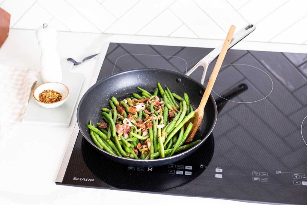 A skillet with green beans and fried bacon shown on a Sharp Induction Cooktop.