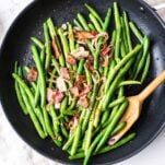 A close up look at bacon green beans in a black skillet.