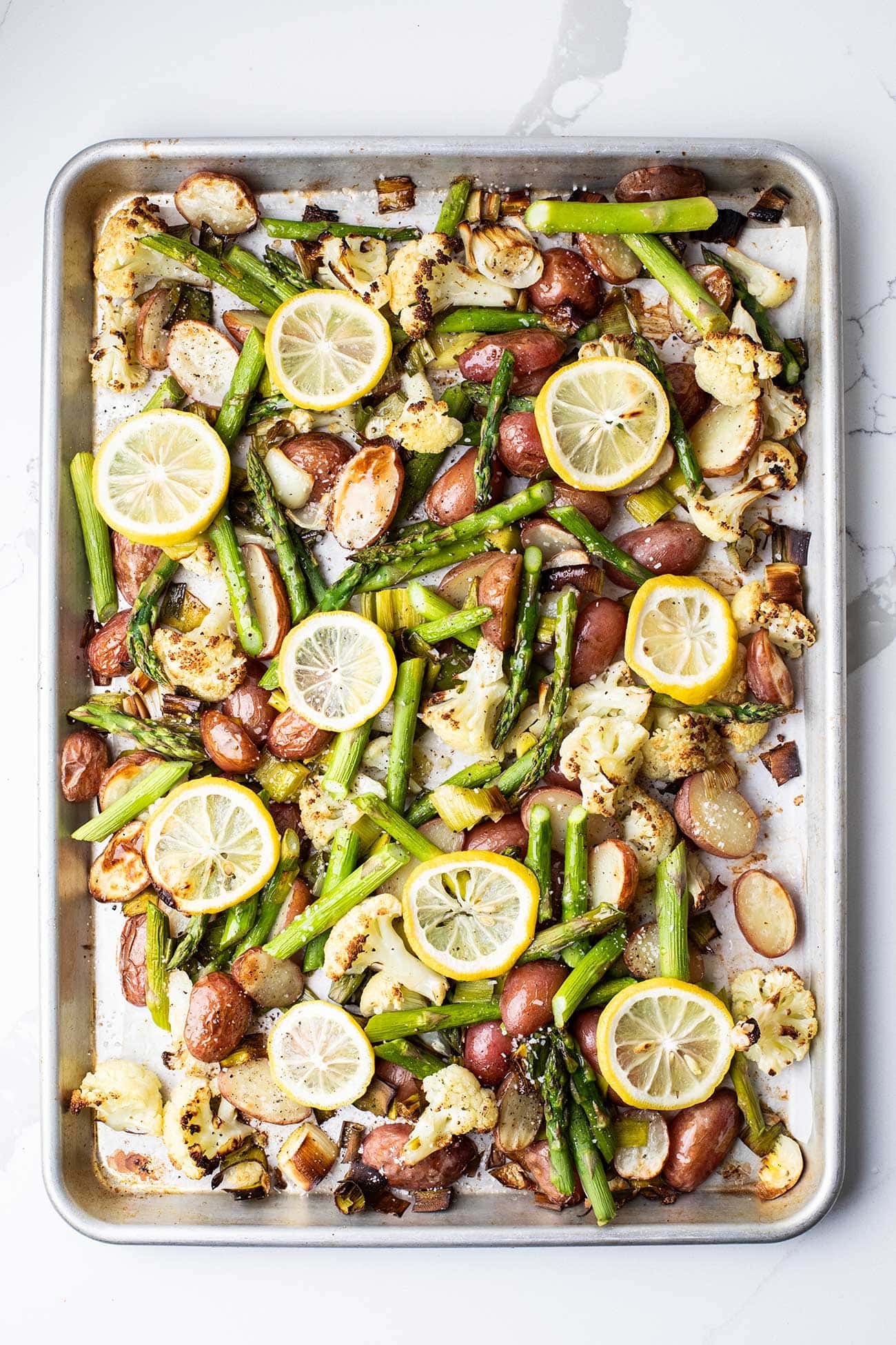 A sheet pan showing roasted vegetables topped with lemon slices.