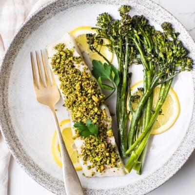 A plate shown with pistachio crusted halibut and roasted baby broccoli.